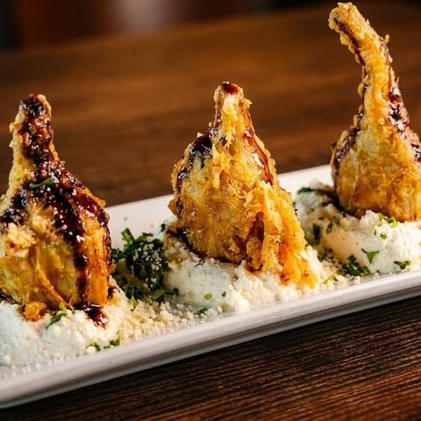 Three fried artichoke hearts drizzled with balsamic glaze, served on a bed of ricotta cheese.