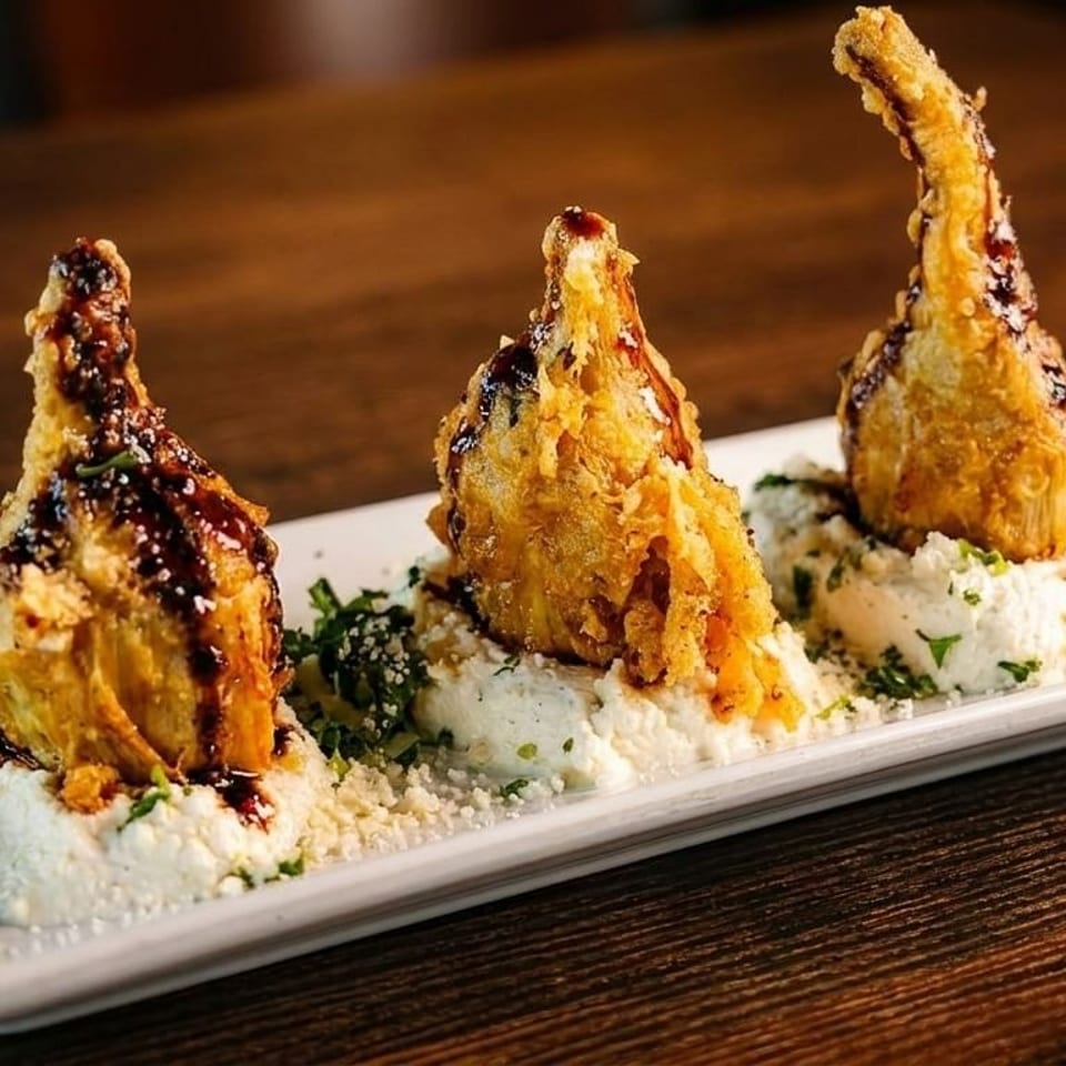 Three fried artichoke hearts drizzled with balsamic glaze, served on a bed of ricotta cheese.