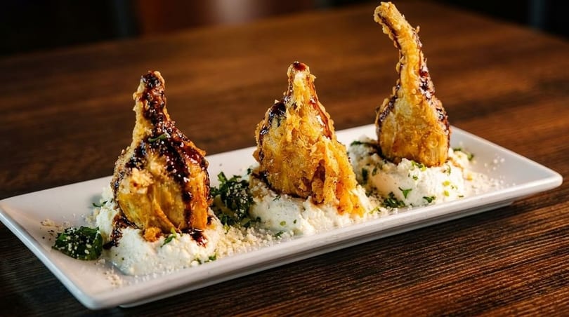Three fried artichoke hearts drizzled with balsamic glaze, served on a bed of ricotta cheese.